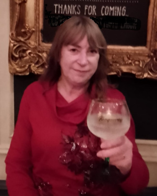 A Photograph of Diana holding a wine glass, wearing a fancy red sweater. She's got shoulder length brown hair, peach skin.
